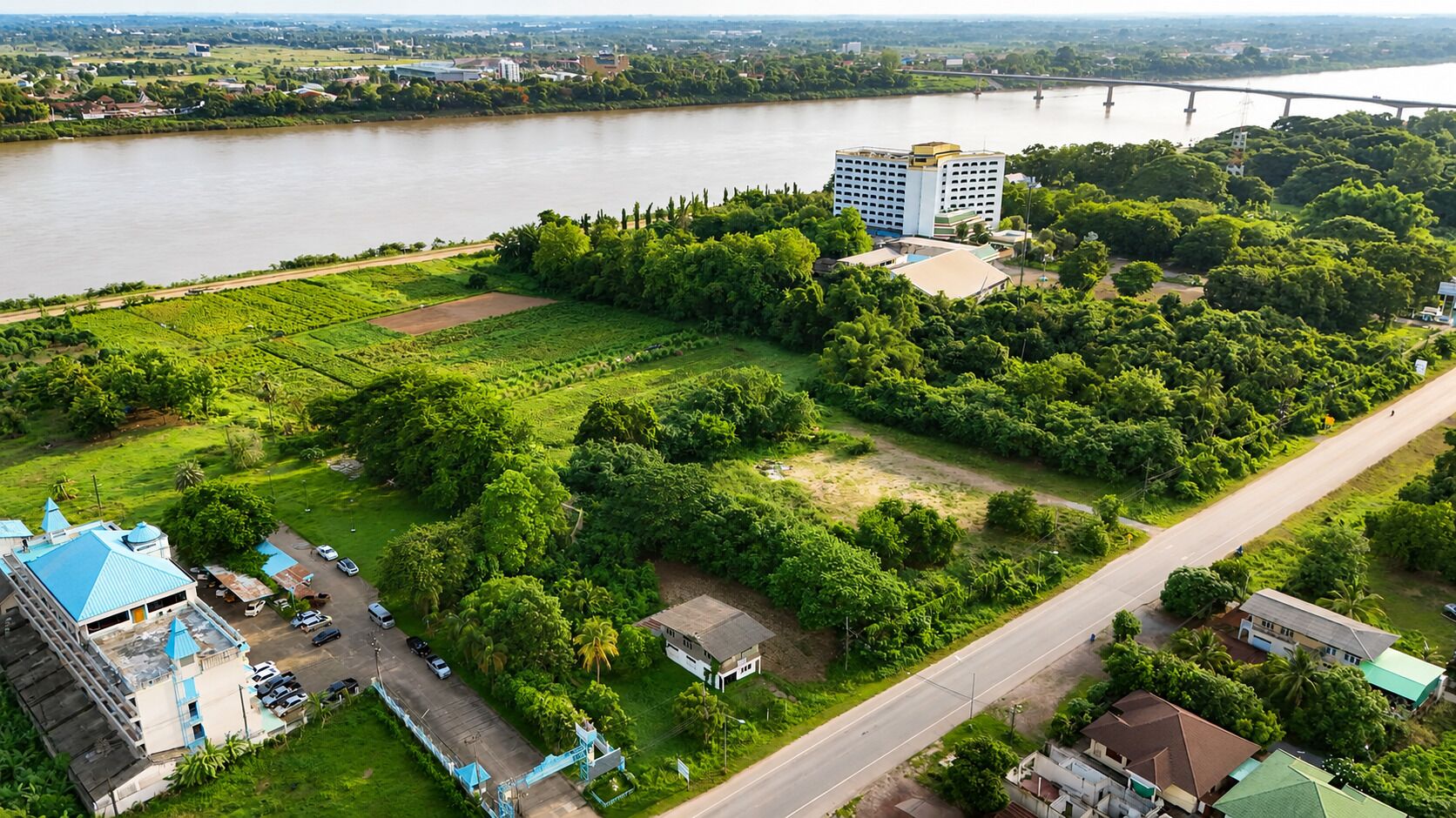 An aerial view of a rural area with a river, a bridge, and a large building with a blue roof.