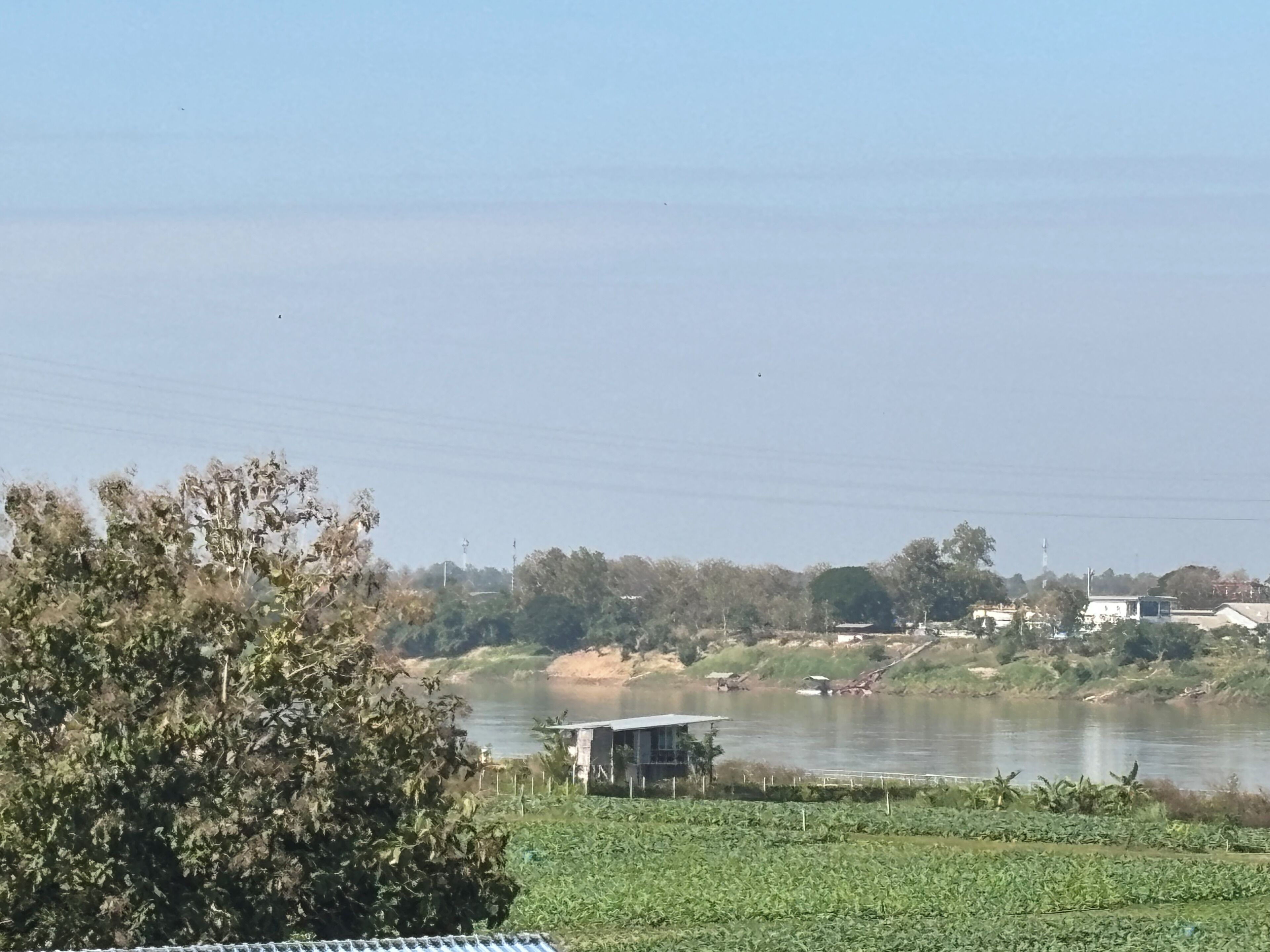 Uitzicht op een rivier met een klein gebouw aan het water, omgeven door groen en bomen.