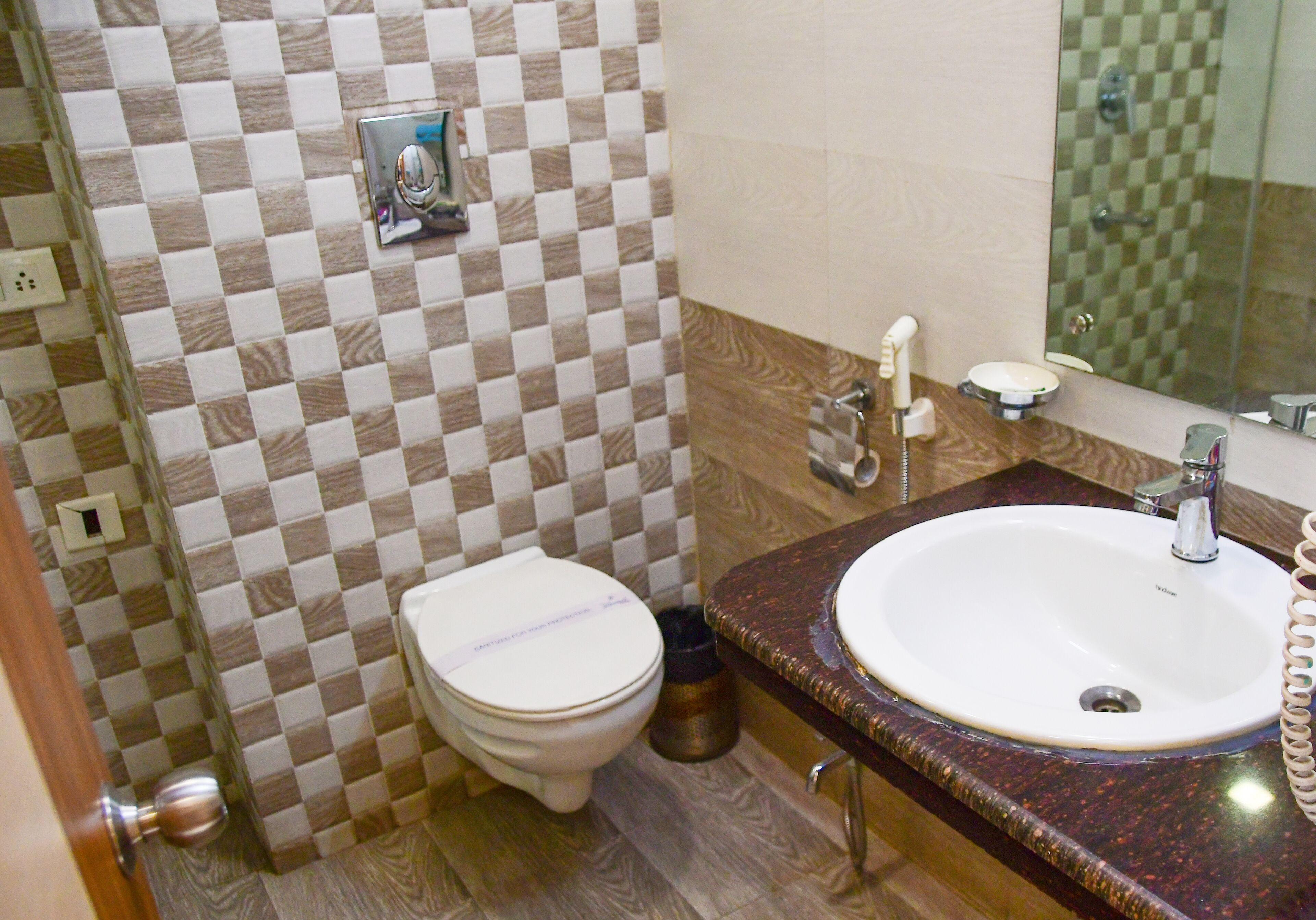 Une salle de bain avec un mur recouvert de carreaux à motifs, des toilettes blanches, un lavabo avec un miroir et un espace douche.