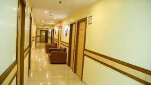 Un pasillo de hotel con suelo de mármol, puertas de madera y una zona de estar con sillas marrones.