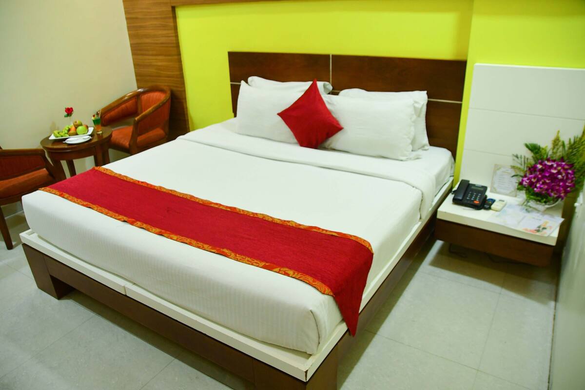 Quarto de hotel com uma cama, mesa de cabeceira, uma cadeira e uma pequena mesa com uma fruteira.
