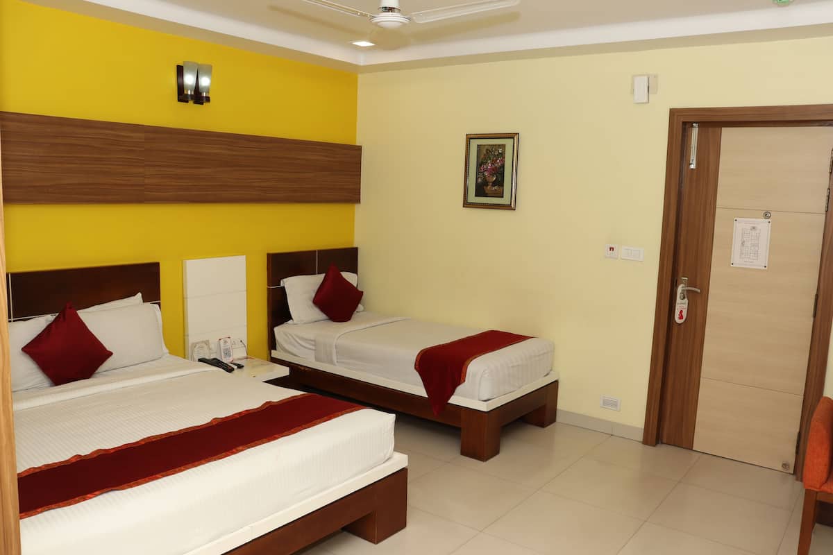 Quarto de hotel com duas camas de solteiro, cabeceira de madeira, luminária fixada na parede, porta com puxador e pequena moldura com uma imagem na parede.
