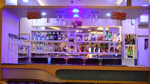 Zona de bar con estantes llenos de botellas de licor, vasos y un letrero de neón.