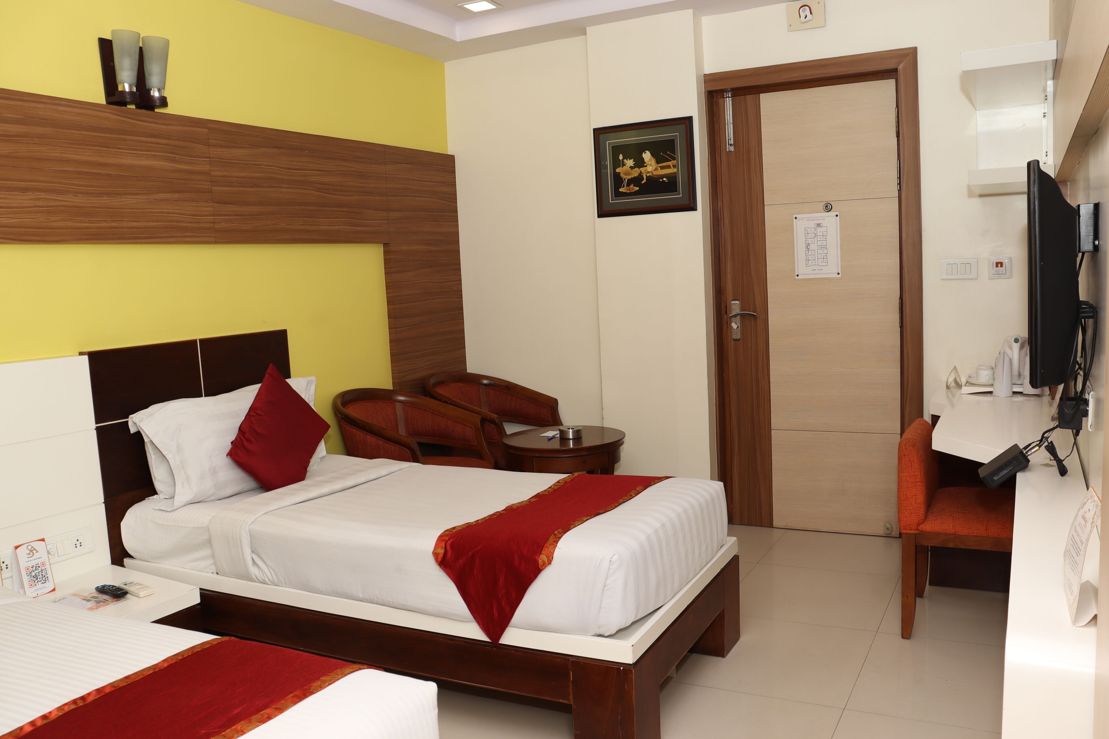Una habitación de hotel con cama, escritorio, silla, televisor y puerta.