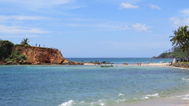 A beach with clear water, a sandy shore, and a rocky cliff. - Sailors Mirissa (Mirissa)
