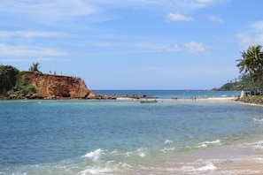 A beach with clear water, a sandy shore, and a rocky cliff. - Sailors Mirissa (Mirissa)