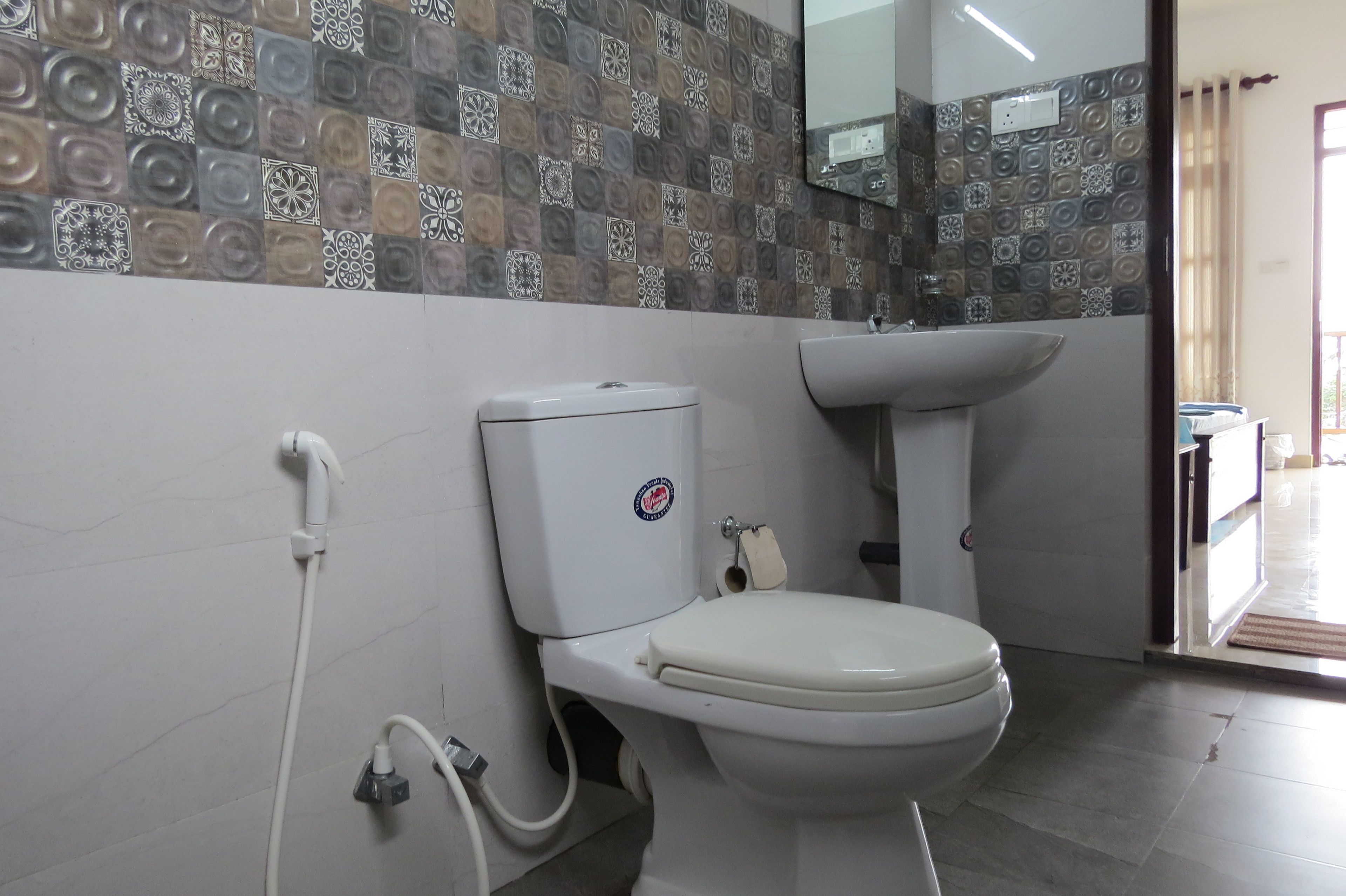 A bathroom with a toilet, sink, and patterned tiles on the wall.