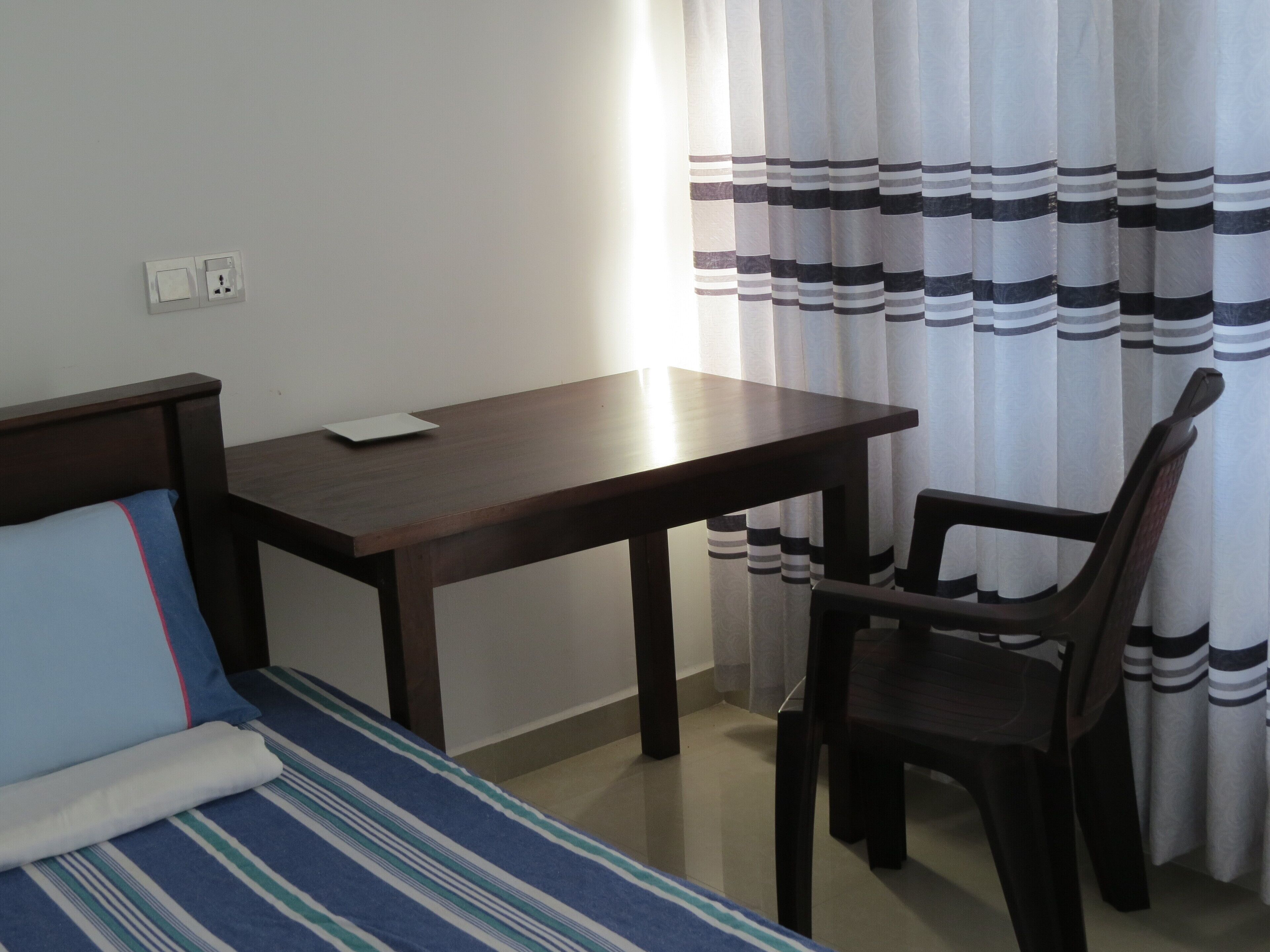 A room with a bed, a desk, and a chair. There is a power outlet on the wall.