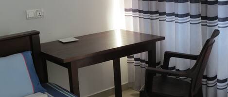 A room with a bed, a desk, and a chair. There is a power outlet on the wall.