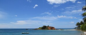 A beach with clear blue water, a small boat, and a rocky island with palm trees. - Sailors Mirissa (Mirissa)