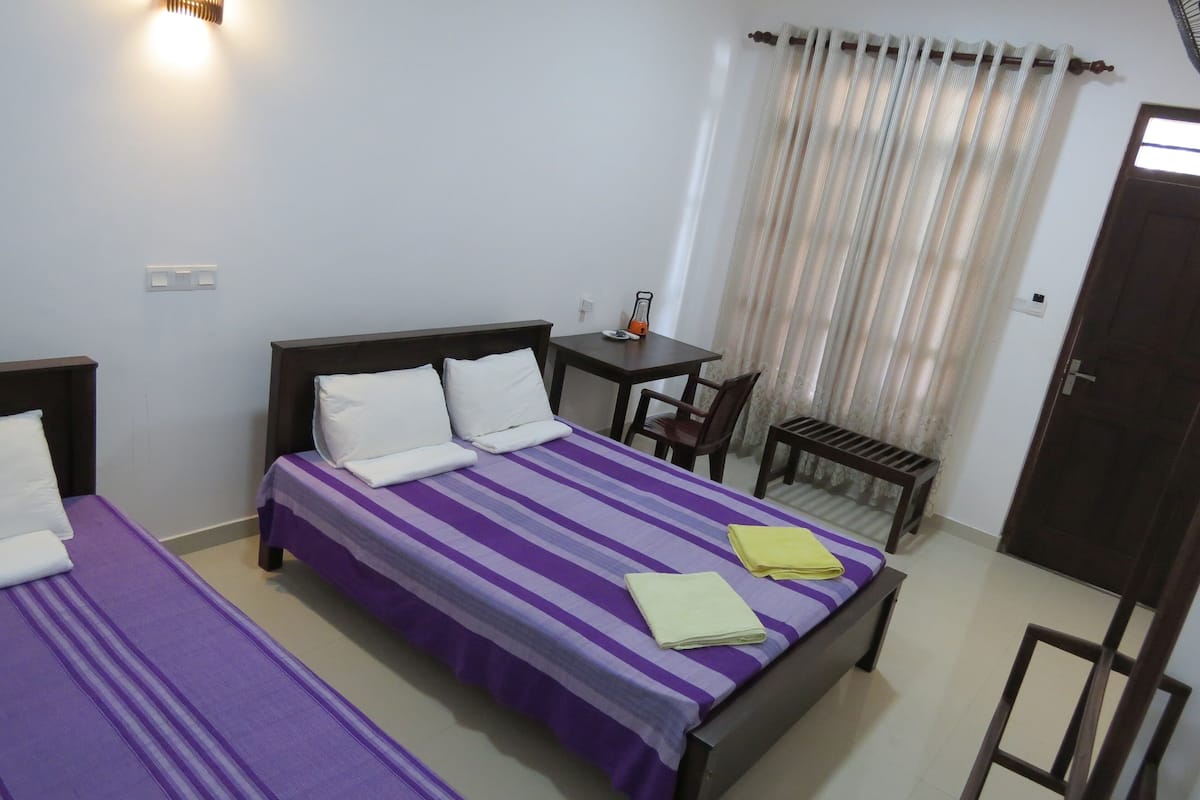 A room with two beds, a small table, a chair, and a window with curtains.