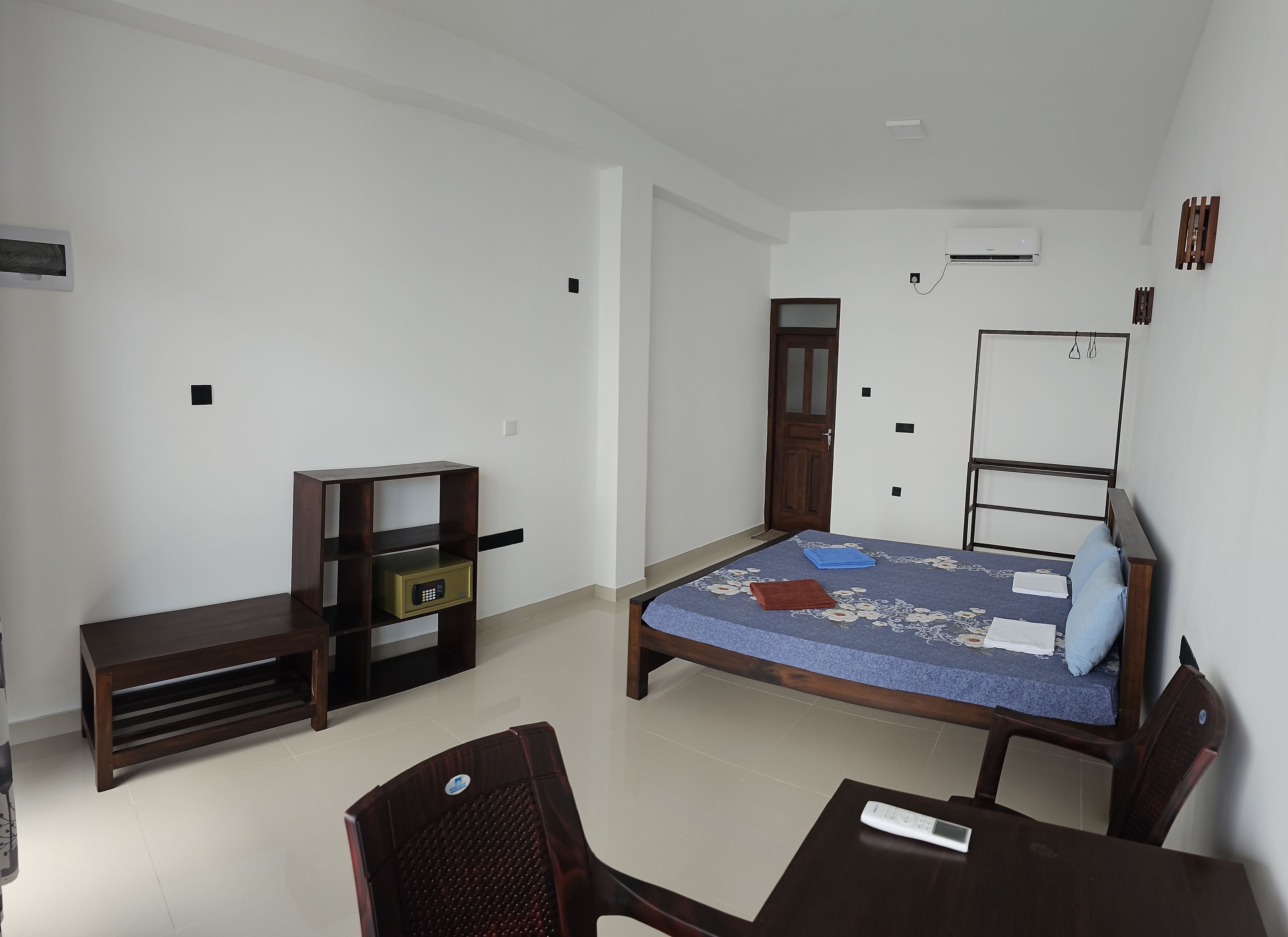 A small, well-lit room with a bed, a desk, a chair, and a TV stand.