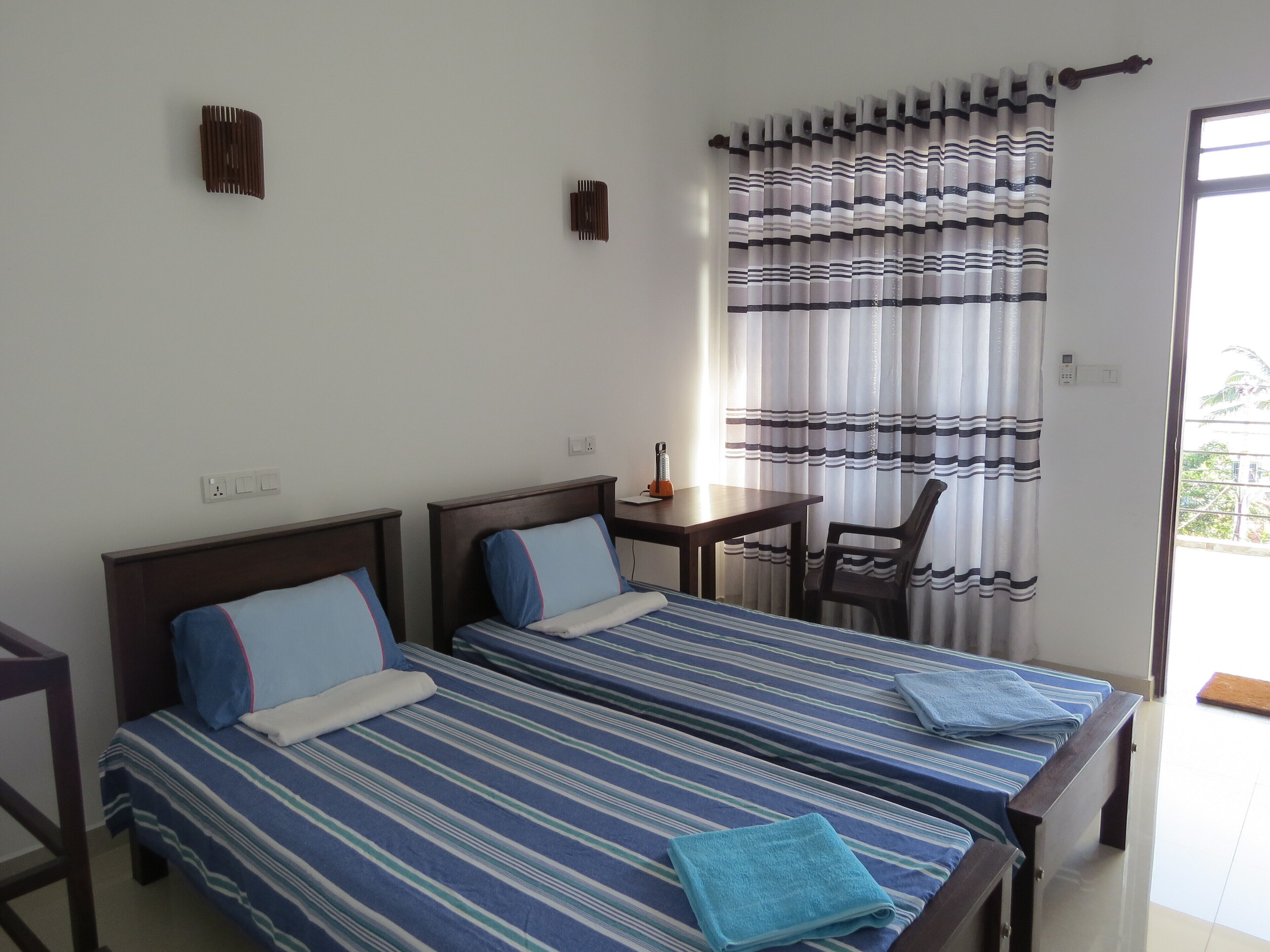 Una habitación con dos camas, una mesita, una silla y un ventanal con cortinas a rayas.