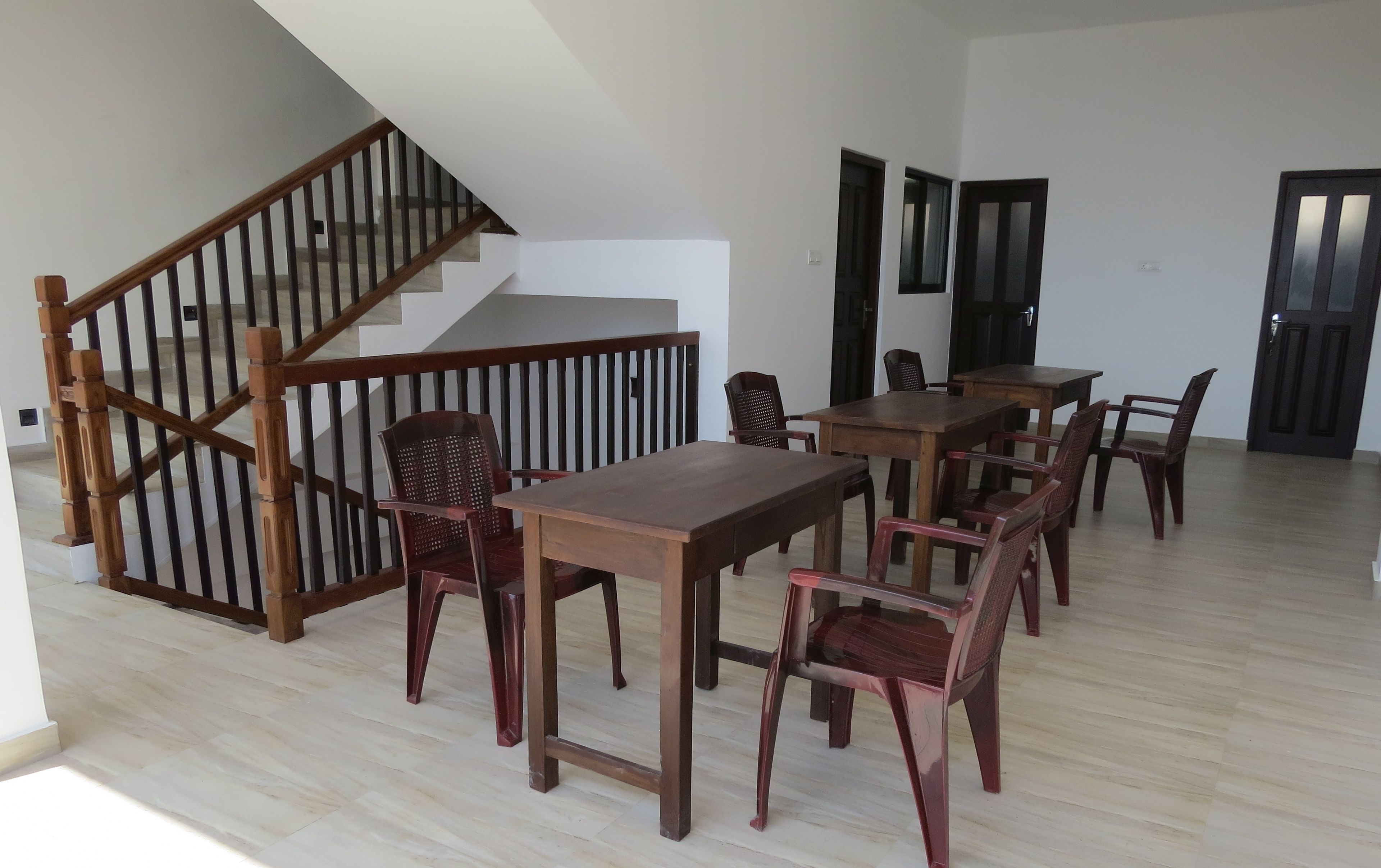 Amplia habitación con escalera de madera, zona de comedor con mesas y sillas de madera, y un gran ventanal que proporciona luz natural.