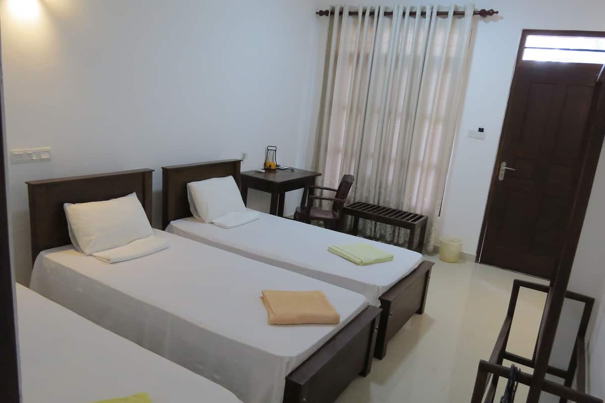 A room with two beds, a small table, a chair, a window with curtains, and a door.