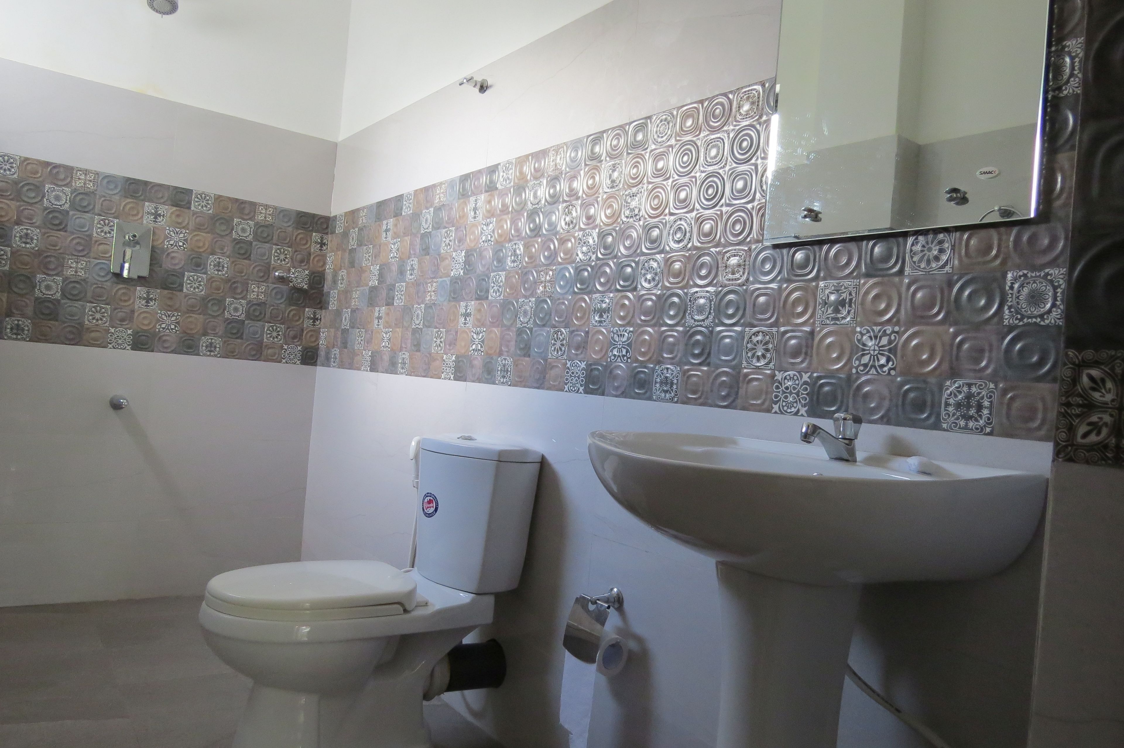 Un baño con inodoro, lavamanos y azulejos con diseño.