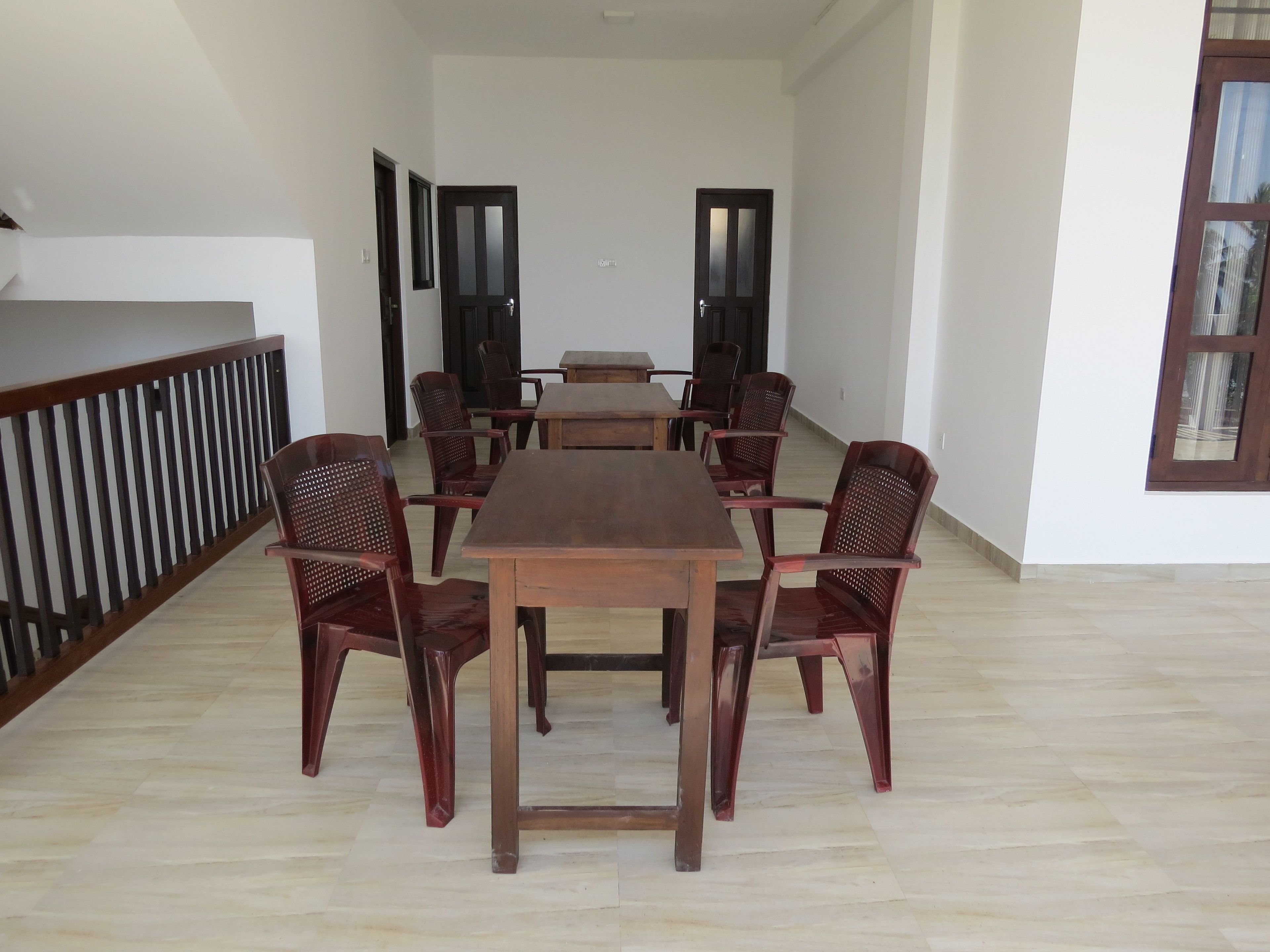 A spacious dining area with a long wooden table and six chairs, a wooden railing on one side, and a large window on the right.