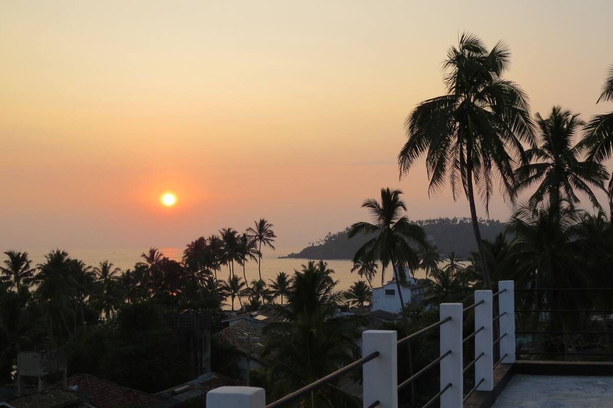 A sunset view with palm trees and a distant hill.