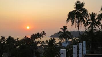 A sunset view with palm trees and a distant hill.