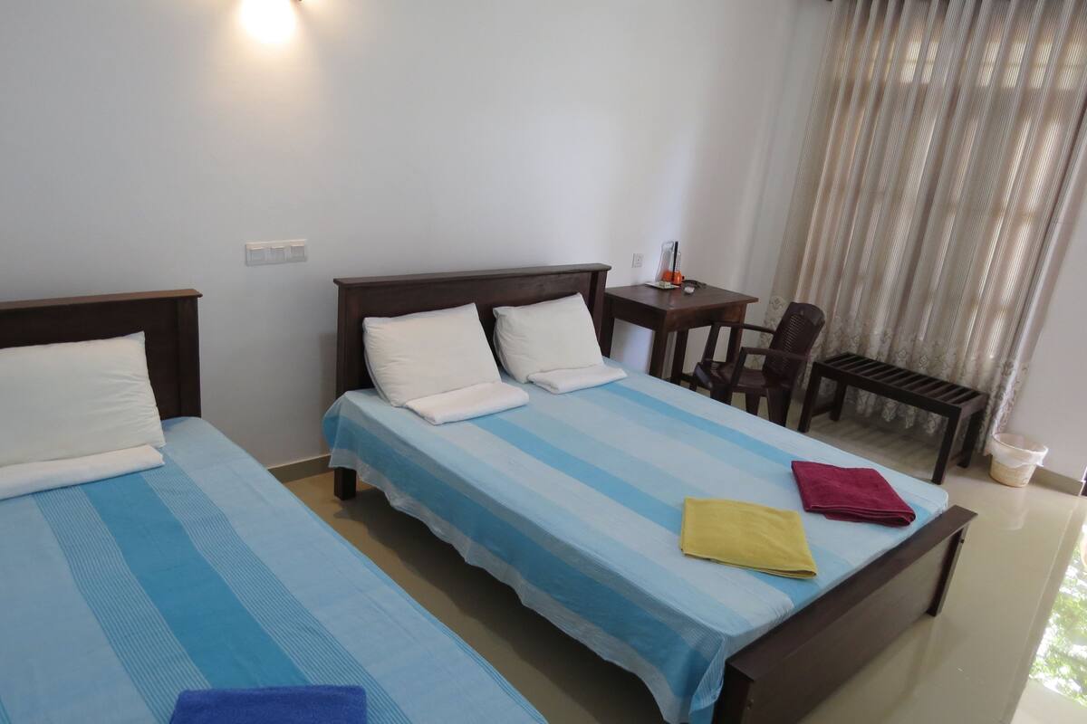 A hotel room with two beds, a small table, a chair, and a window with curtains.