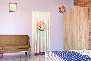A room with a sofa, a bed with a patterned bedspread, a wooden wardrobe, a door with a circular design, and a clock on the wall. - Sleepy Lagoon (Pak Chong)