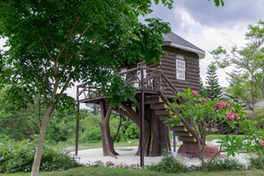 A treehouse with a wooden exterior, built into a large tree, featuring a small window and a wooden staircase. - Sleepy Lagoon (Pak Chong)