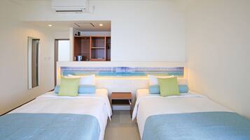 A hotel room with two beds, a small table, a mirror, and a kitchenette area.