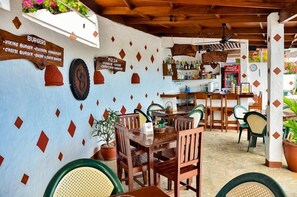 A restaurant with wooden tables and chairs, a bar area with a Coca-Cola refrigerator, and a menu board listing burgers and pizza.