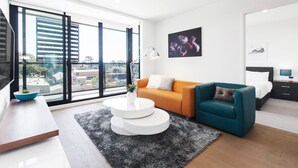 Una sala de estar moderna con un sofá, una mesa de centro y vistas de la ciudad a través de amplios ventanales.