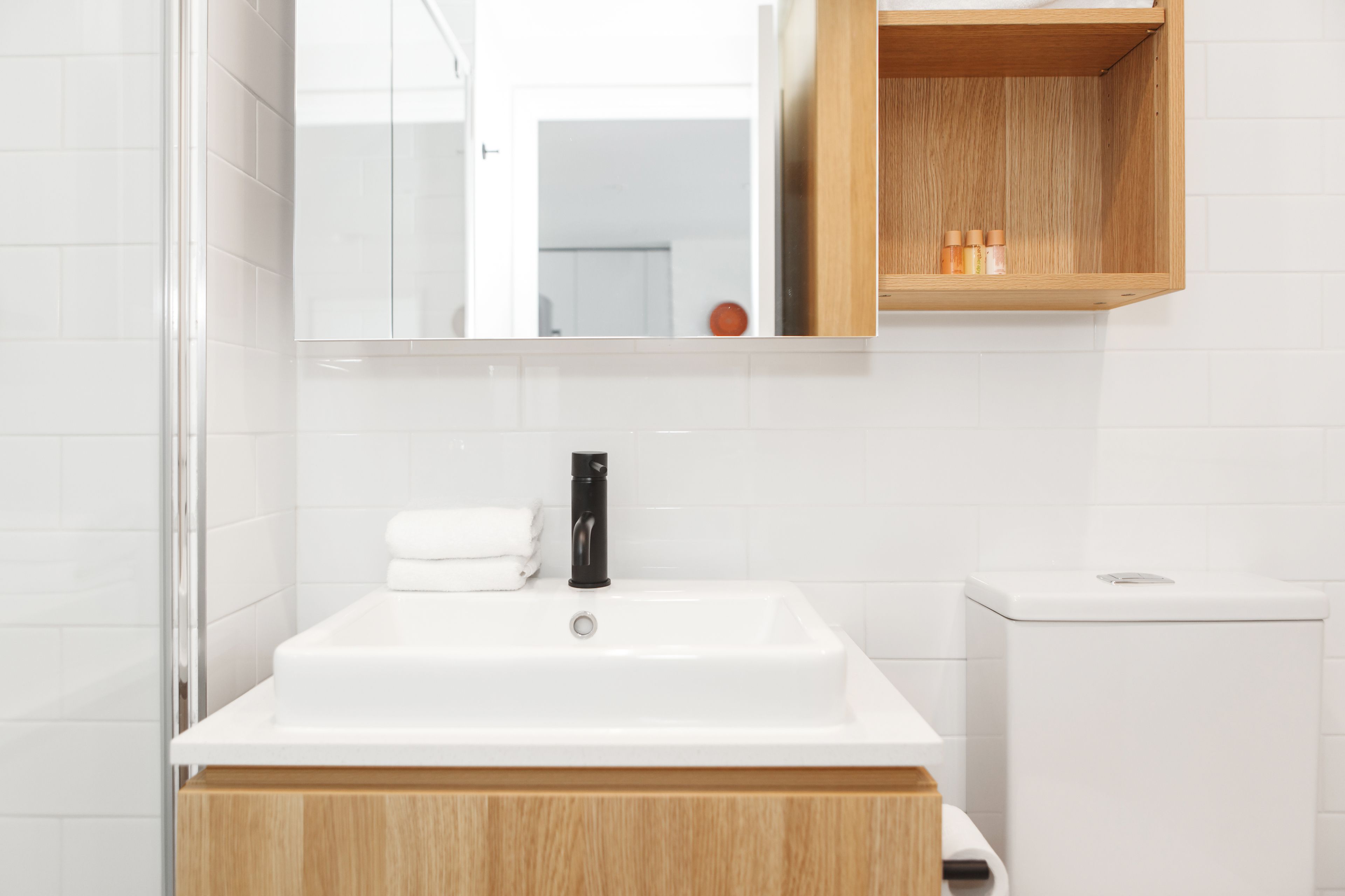 A bathroom with a white sink, a mirror, a wooden cabinet, and a toilet.