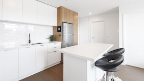 Una cocina moderna con armarios blancos, un refrigerador de acero inoxidable y una encimera blanca.