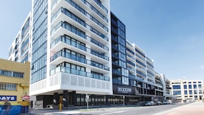 Un edificio moderno de varios pisos con balcones y ventanas grandes, con la leyenda "ILIXIR APARTMENTS".
