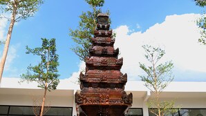 Une structure en pierre à plusieurs niveaux, située dans une cour agrémentée de plantes en pot, avec un bâtiment moderne en arrière-plan.