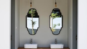 Une salle de bain moderne avec deux vasques, un banc en bois et deux miroirs muraux ornés de motifs représentant des arbres.