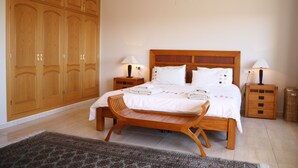 A bedroom with a large wooden wardrobe, a bed with white linens, two bedside tables with lamps, and a wooden bench. - Spacious villa, close to Denia, Pool 10m x 5m, great views, A/C, fast wifi 500mb (Alicante)