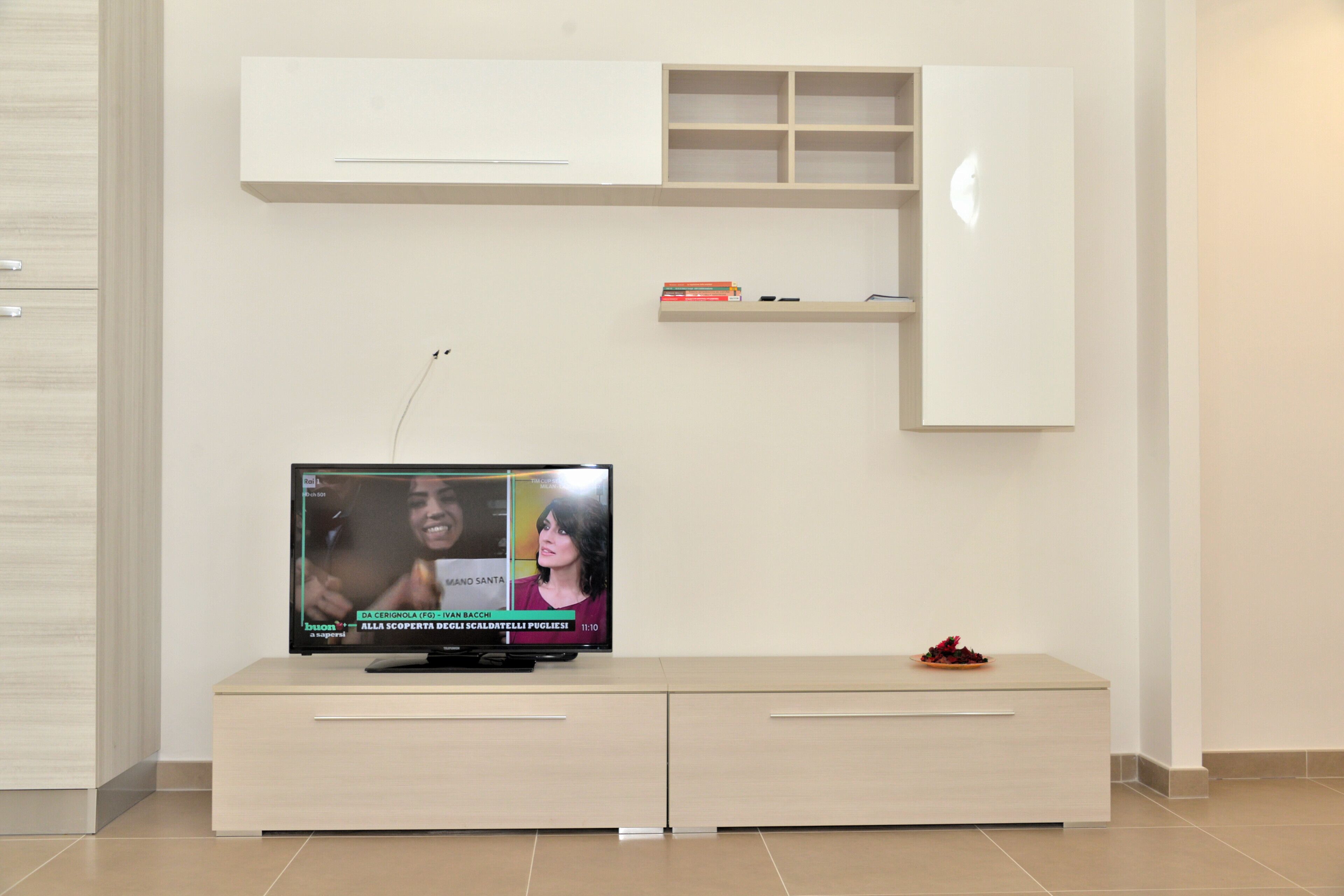 A flat-screen TV on a modern cabinet with a shelf above it.