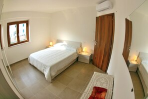 A bedroom with a bed, bedside tables, a wooden wardrobe, a window, and an air conditioning unit.