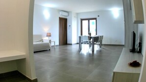 A spacious living area with a dining table and chairs, a sofa, and a TV on a stand. - Blue apartment (Rodi Garganico)