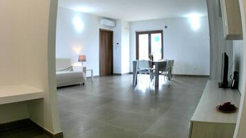 A spacious living area with a dining table and chairs, a sofa, and a TV on a stand.