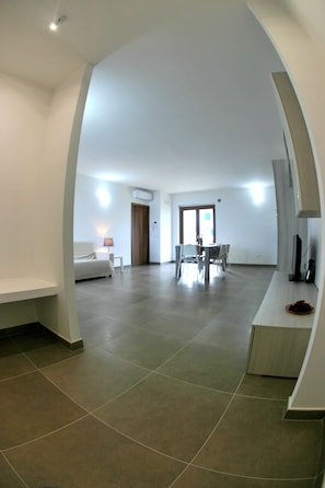 A spacious living area with a dining table and chairs, a sofa, and a TV on a stand.