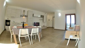 A modern kitchen with white cabinetry, a dining table with chairs, and a TV. - Blue apartment (Rodi Garganico)