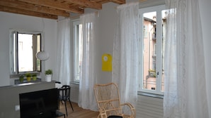 A living room with a TV, a wicker chair, and a window with white curtains. - NEW APARTMENT in the heart of Citta 'Alta (Bergamo)
