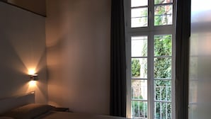 A bedroom with a bed, a wall-mounted light, and a large window with curtains. - NEW APARTMENT in the heart of Citta 'Alta (Bergamo)