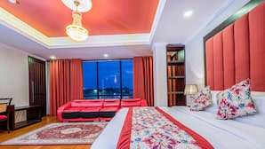 Ein Schlafzimmer mit einem großen Bett, einem roten Sofa, einem Kronleuchter, einem Bücherregal und Blick auf die Stadt bei Nacht.