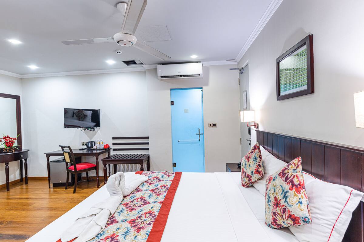 Ein Hotelzimmer mit Bett, Schreibtisch, Sessel, Fernseher und Deckenventilator.