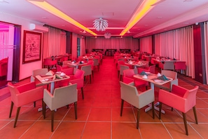A restaurant with red and white decor, multiple tables and chairs, and a central chandelier.
