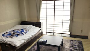 A small room with a bed, a table, and a window with a grid pattern.