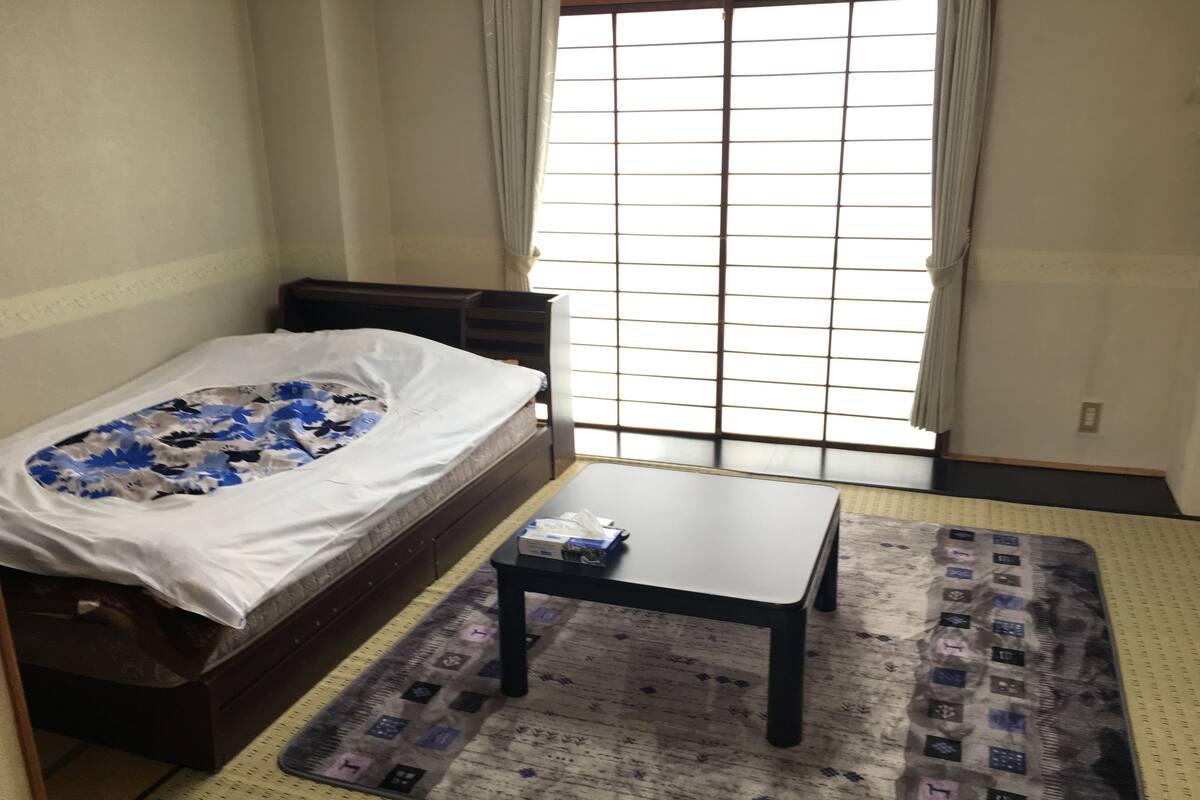 Une petite pièce comprenant un lit, une table et une fenêtre à carreaux.