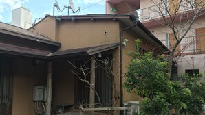 A residential building with satellite dishes, a wooden porch, and a small garden area.