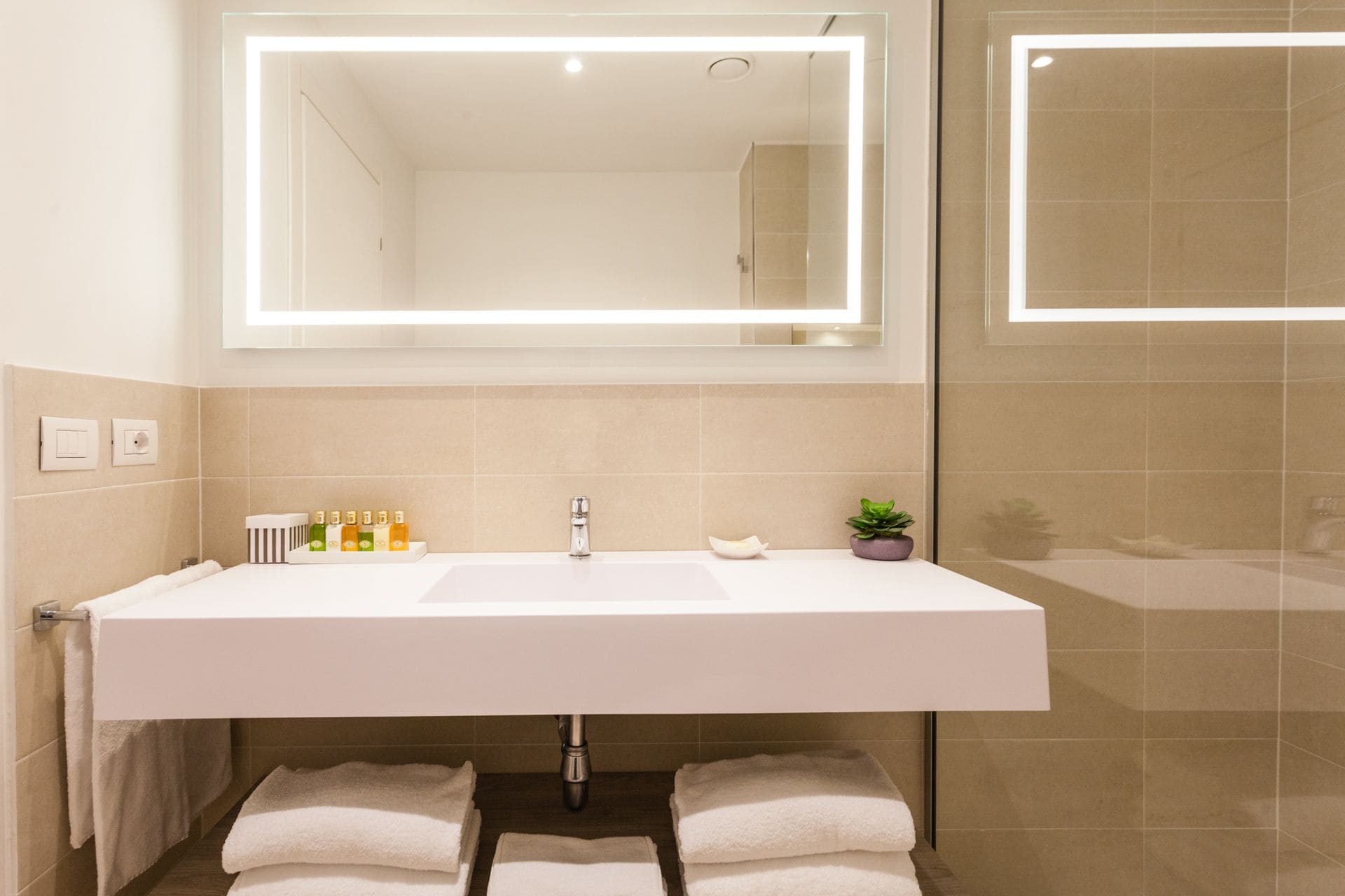 Un baño moderno con un espejo grande, un lavamanos blanco y un perchero para toallas.